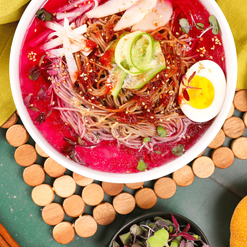 Pink noodle soup with avocado, egg, radish, and chili sauce